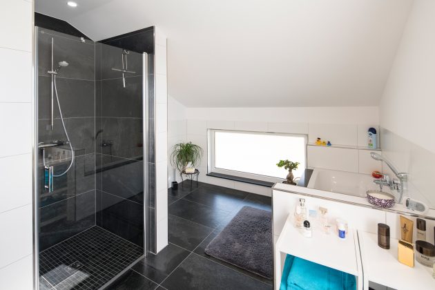 Badezimmer: Eine Fensterfolie schützt vor neugierigen Einblicken. Die dunklen Bodenfliesen ähneln denen eine Etage tiefer. Als Mosaik liegen sie in der Dusche. (Foto: FingerHaus)